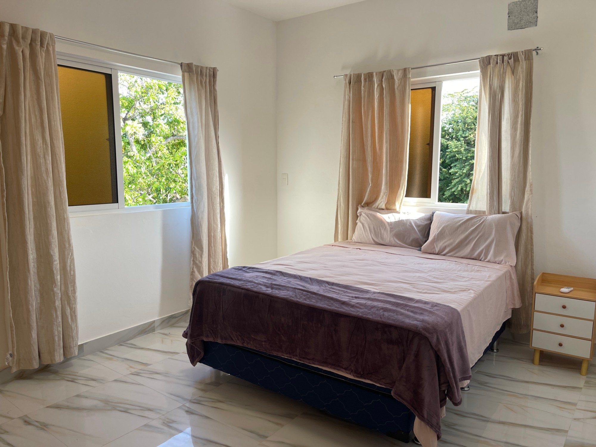 A bedroom with windows on two sides looking into the trees